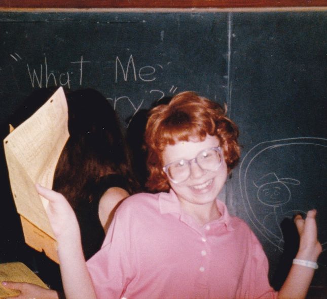blog author wearing glasses standing in front of chalkboard in 6th grade class